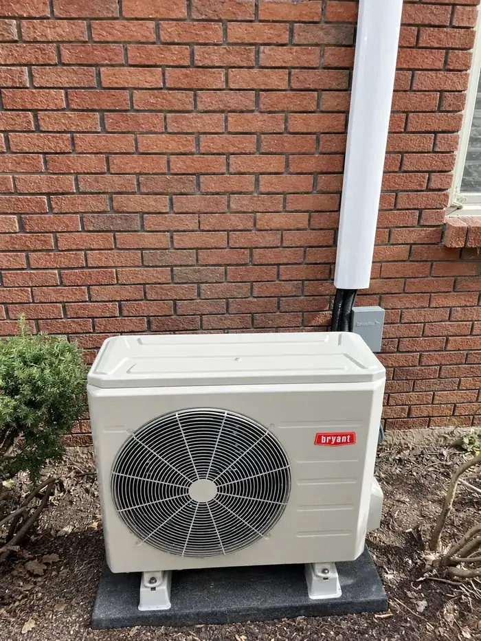 A Bryant ductless outdoor unit mounted beside a brick wall